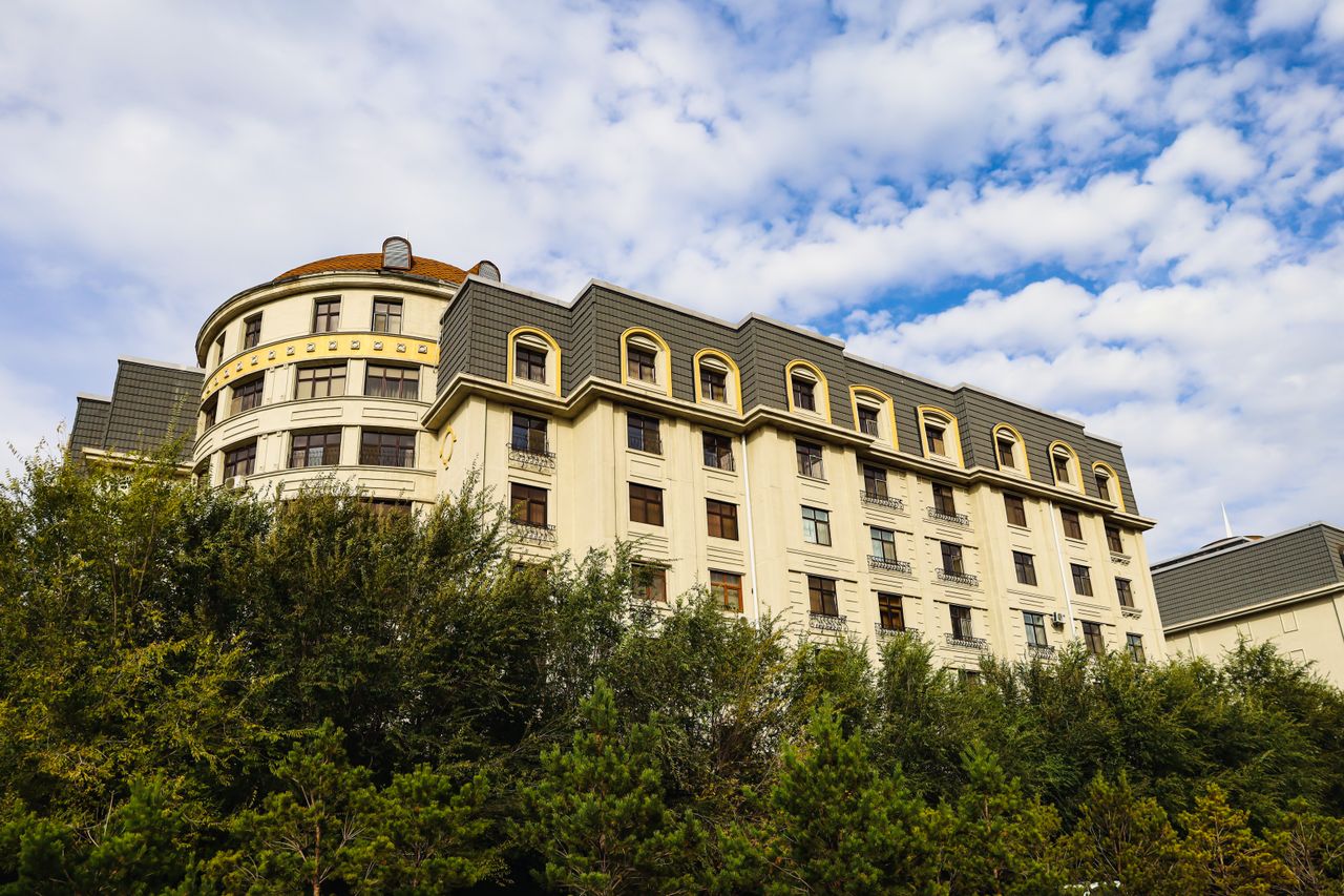 A stylish multi-storey hotel exterior with lush greenery and a vibrant cloudy sky backdrop.